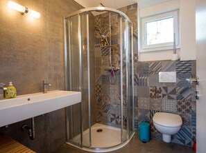 Een badkamer met een douchecabine met glazen wanden, een witte wastafel, een toilet en betegelde vloeren.