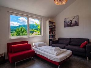 A bedroom with a bed, a red sofa, a dark sofa, a bookshelf, and a painting of an elk.
