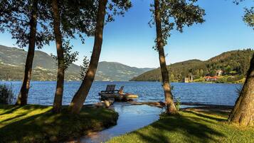 A lakeside view with a dock, trees, and a distant house.