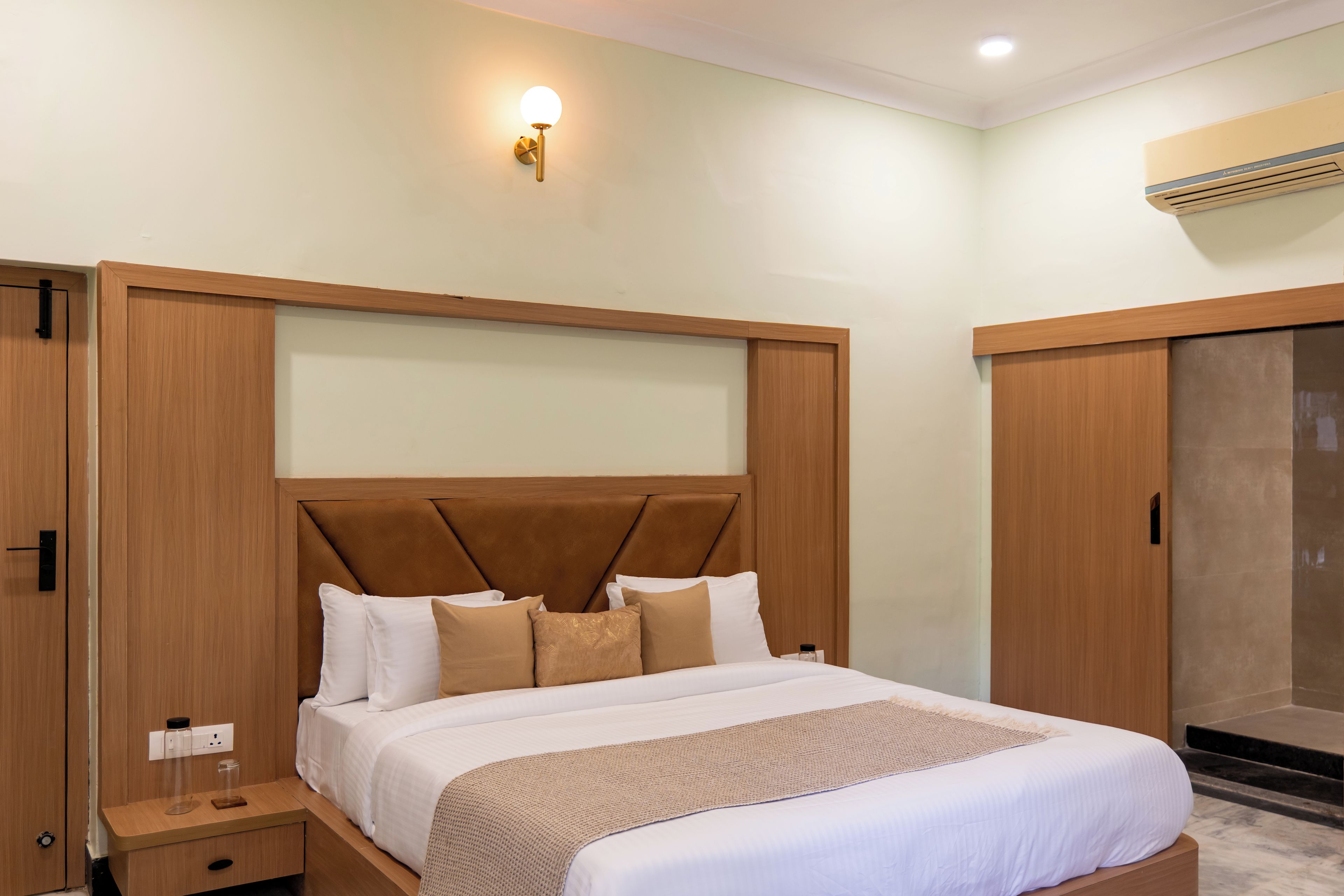 A hotel room with a large bed, wooden headboard, bedside tables, and a wall-mounted light fixture.