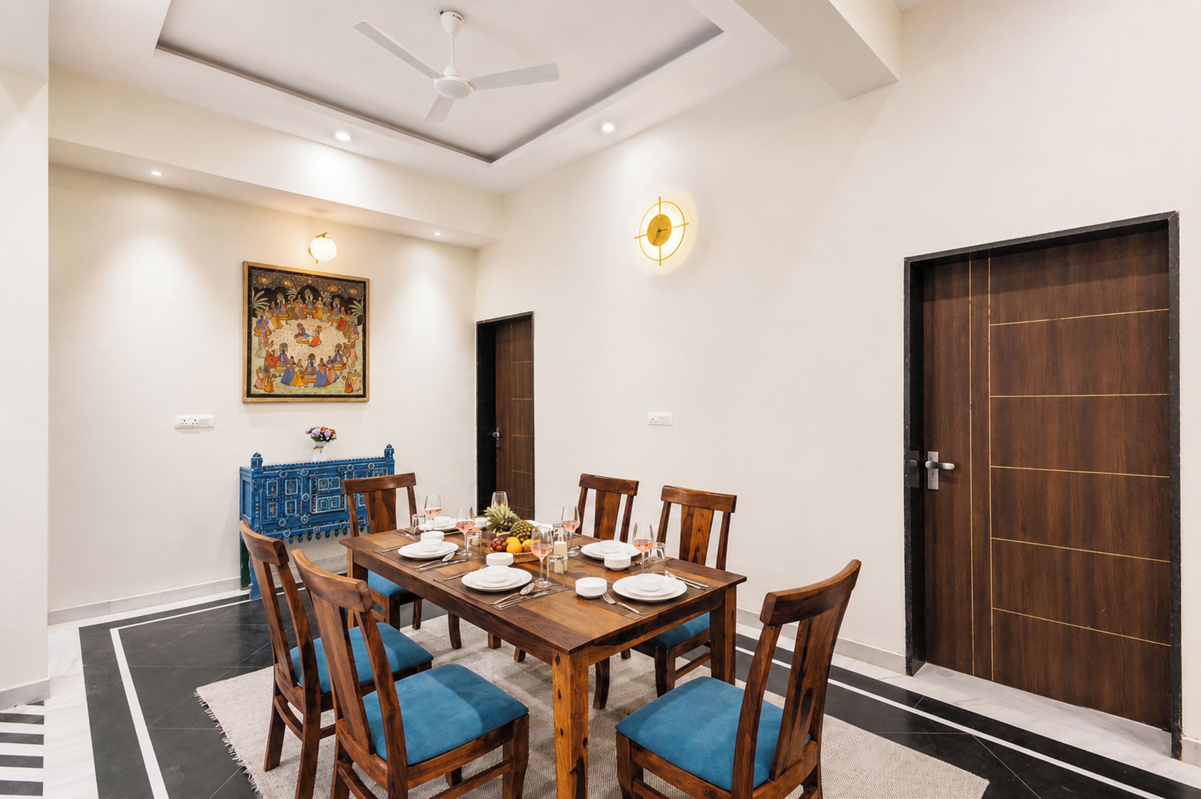 A dining room with a wooden table set for four, surrounded by blue upholstered chairs.