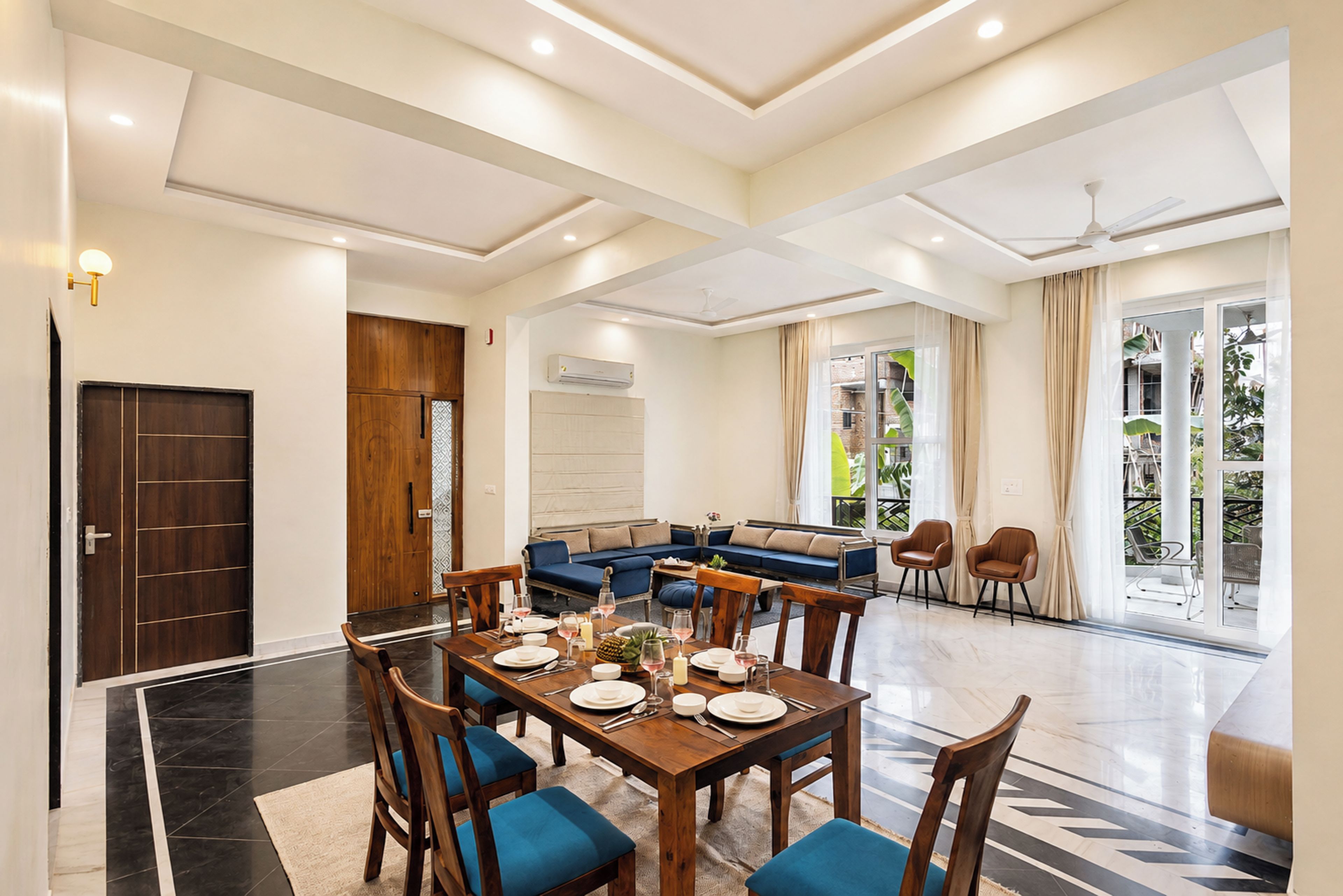 Amplia sala de estar con una mesa de comedor preparada para cuatro personas, un sofá azul y un balcón con sillas.