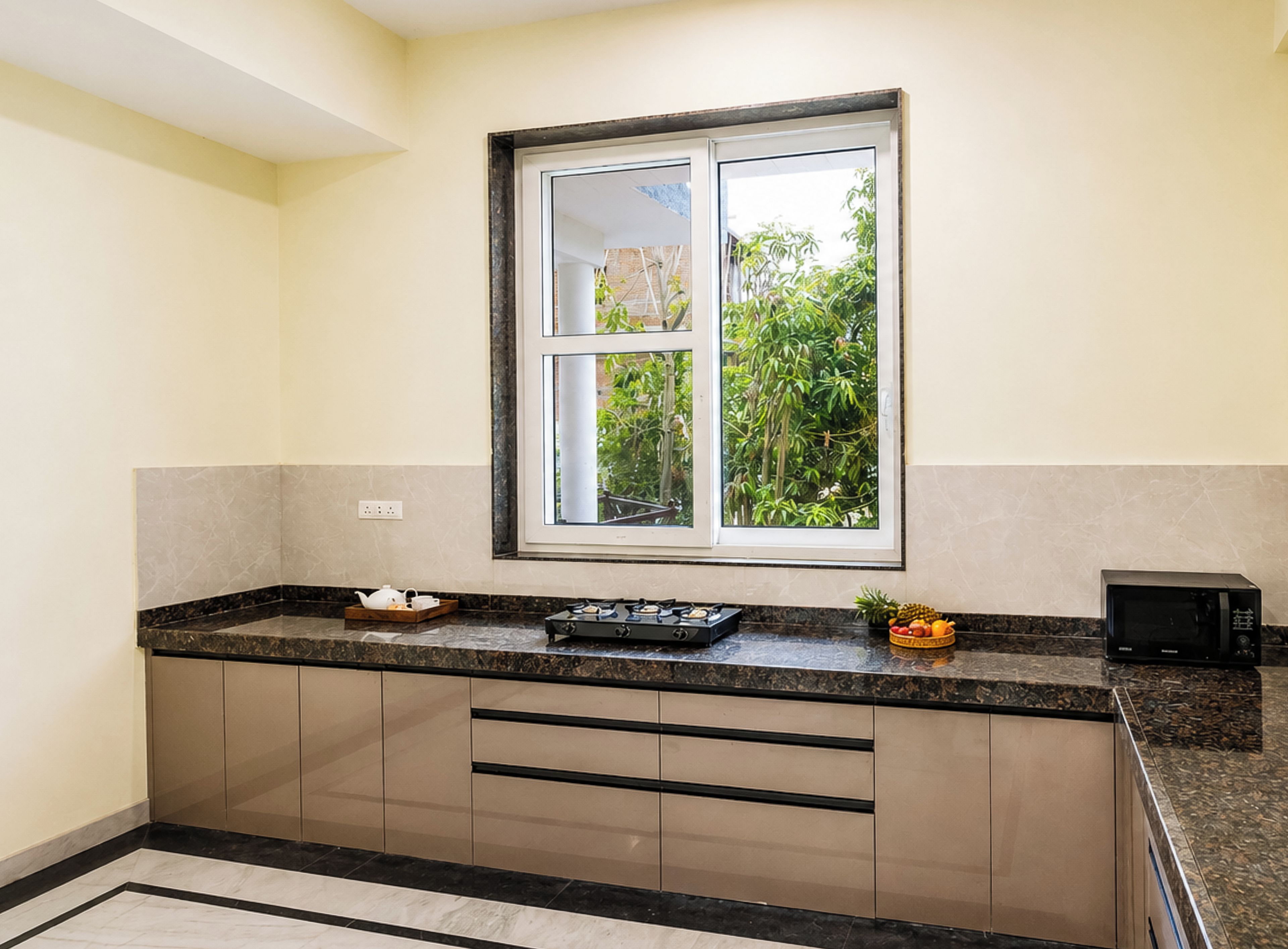 A kitchen with a window, cabinets, countertop, and a microwave.