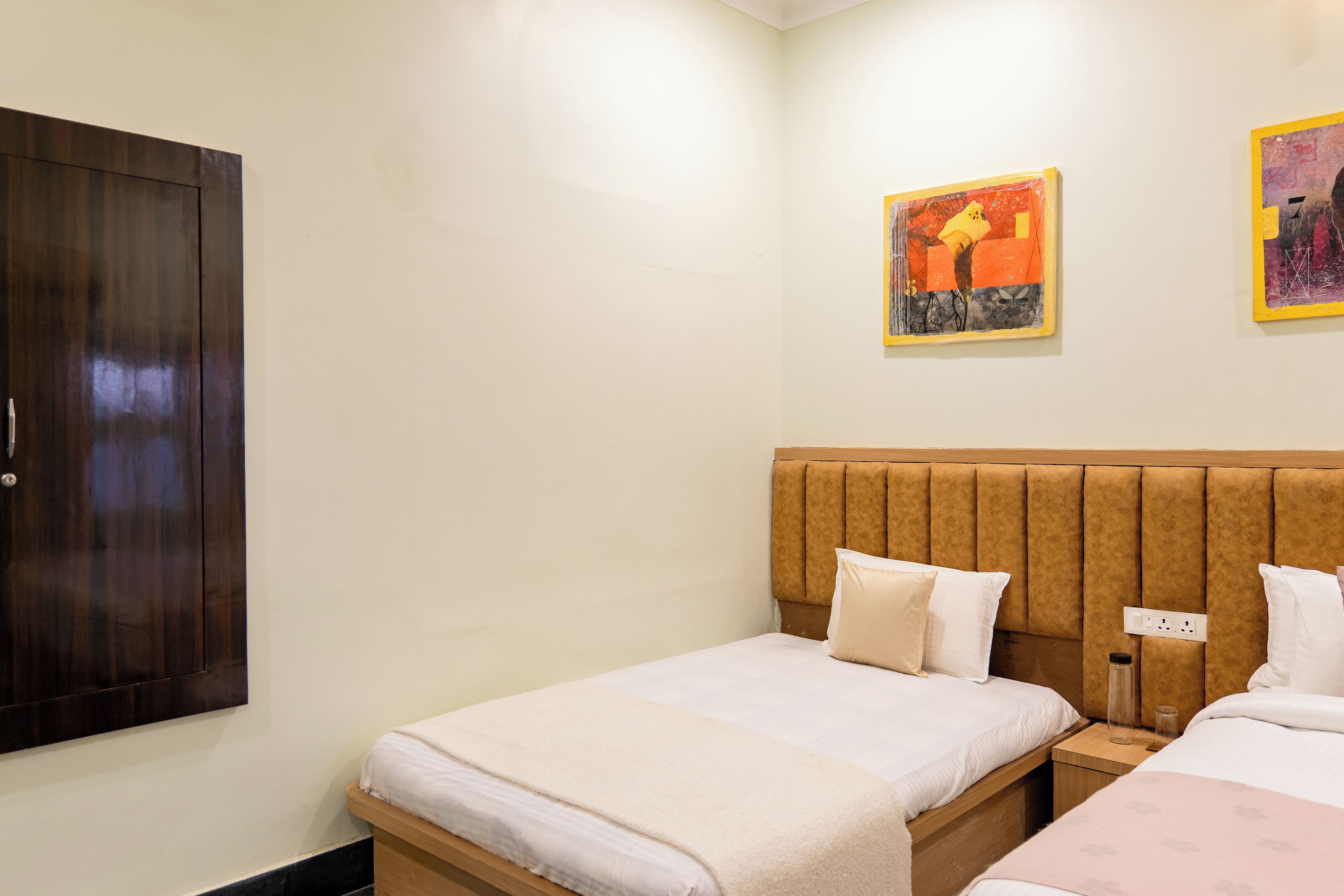 A hotel room with a wooden wardrobe, a bed with a headboard, and two paintings on the wall.