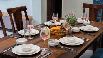Una mesa de comedor dispuesta con platos, vasos, cubiertos y una cesta de frutas.