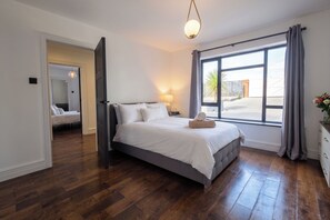 A bedroom with a large bed, a nightstand, a lamp, and a window with curtains. - House Sleeps 11 With Outdoor Pool (Lymington)