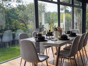 A dining area with a table set for six, chairs, and a view of greenery outside. - House Sleeps 11 With Outdoor Pool (Lymington)