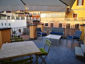 An outdoor patio area with a table and chairs, a covered seating area, and a view of adjacent buildings. - Copy of President Gardens (Rome)