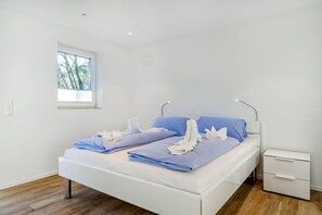 Ein modernes Schlafzimmer mit einem weißen Bett, blauer Bettwäsche und einem kleinen Nachttisch.