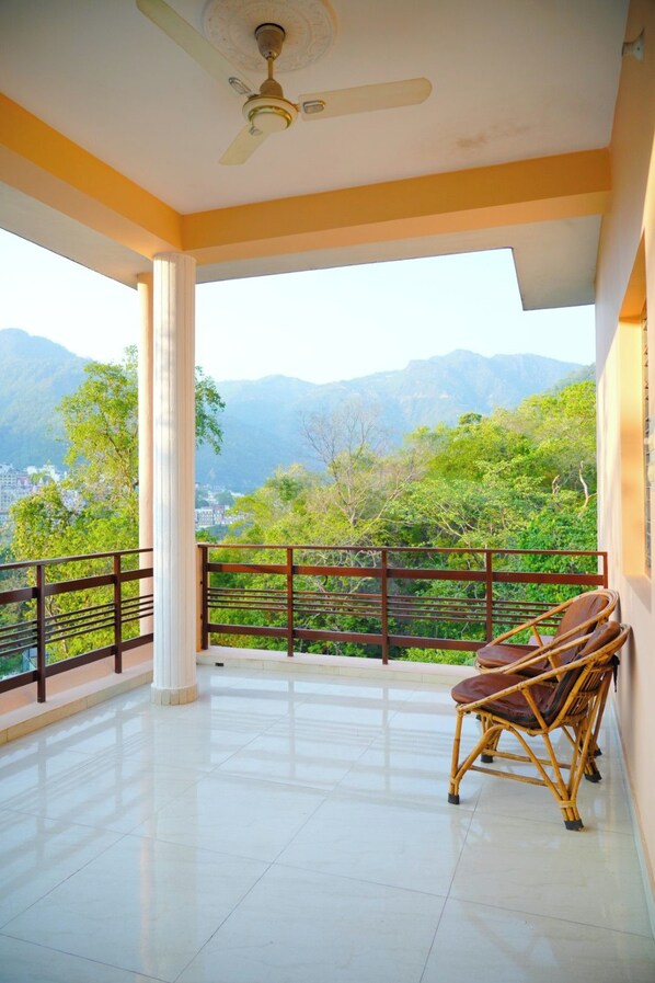 A balcony with a view of mountains, a ceiling fan, and wicker furniture.