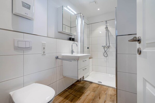 A modern bathroom with a toilet, sink, and shower. - Norderney Vacation Rental (Norden)