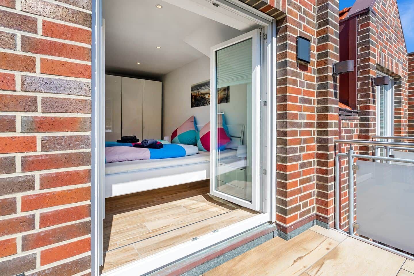A bedroom with a sliding glass door leading to a balcony, a bed with pillows, and a wardrobe.