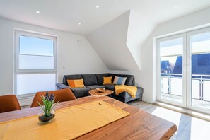 A modern living room with a sofa, a dining table with a vase, and a large window. - Vacation Rental on Langeoog (Norden)
