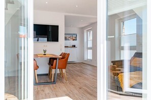 A modern interior with a dining area, kitchen, and a view through a glass door. - Vacation Rental on Langeoog (Norden)