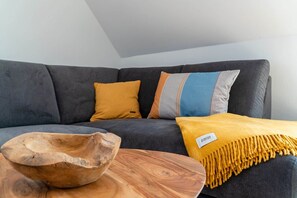 A modern living room with a grey sofa, a wooden bowl, and a yellow throw blanket. - Vacation Rental on Langeoog (Norden)