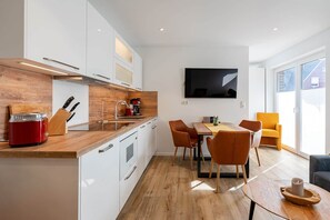 A modern kitchen with a wooden countertop, white cabinets, and a dining area with a table and chairs. - Spiekeroog Vacation Rental (Norden)