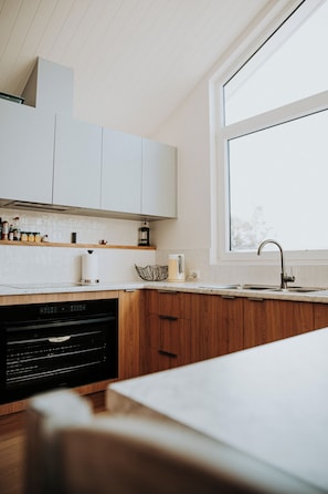A modern kitchen with wooden cabinets, a built-in dishwasher, and a large window providing natural light. - BUSHMERE ~ Gateway to the Bay of Fires at Binalong Bay (Binalong Bay)