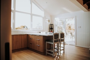 A kitchen with wooden cabinets, a white countertop, and a bar stool. - BUSHMERE ~ Gateway to the Bay of Fires at Binalong Bay (Binalong Bay)