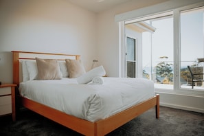 A bedroom with a wooden bed, white bedding, and a large window with a view. - BUSHMERE ~ Gateway to the Bay of Fires at Binalong Bay (Binalong Bay)