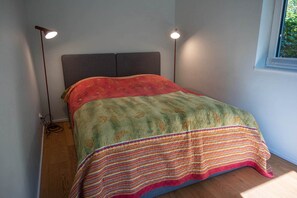 Ein Einzelbett mit Kopfteil, einer gemusterten Tagesdecke und zwei Stehlampen.