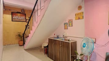 A reception area with a staircase, a wooden counter, a fan, and a potted plant.