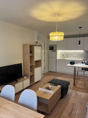 Ein modernes Wohnzimmer mit einem Flachbildfernseher, einem Holztisch und einem Essbereich mit hellem Tisch und Stühlen.
