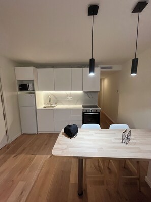 A compact kitchen with white cabinets, a microwave, a refrigerator, a stove, and a dining table with a black bag on it. - Large house in downtown Alicante (Alacant)