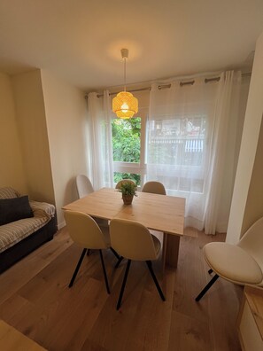 A dining area with a wooden table, four chairs, a hanging light fixture, and a window with curtains. - Large House in Downtown Alicante (Alacant)