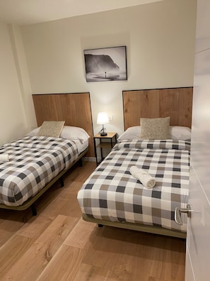 Hotellihuone, jossa on kaksi sänkyä, yöpöytä, lamppu ja seinällä oleva kehystetty kuva.