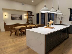 A modern kitchen with a marble island, wooden dining table, pendant lighting, and built-in cabinetry. - New Ultra Luxury Retreat minutes from Arcadia! (Phoenix)