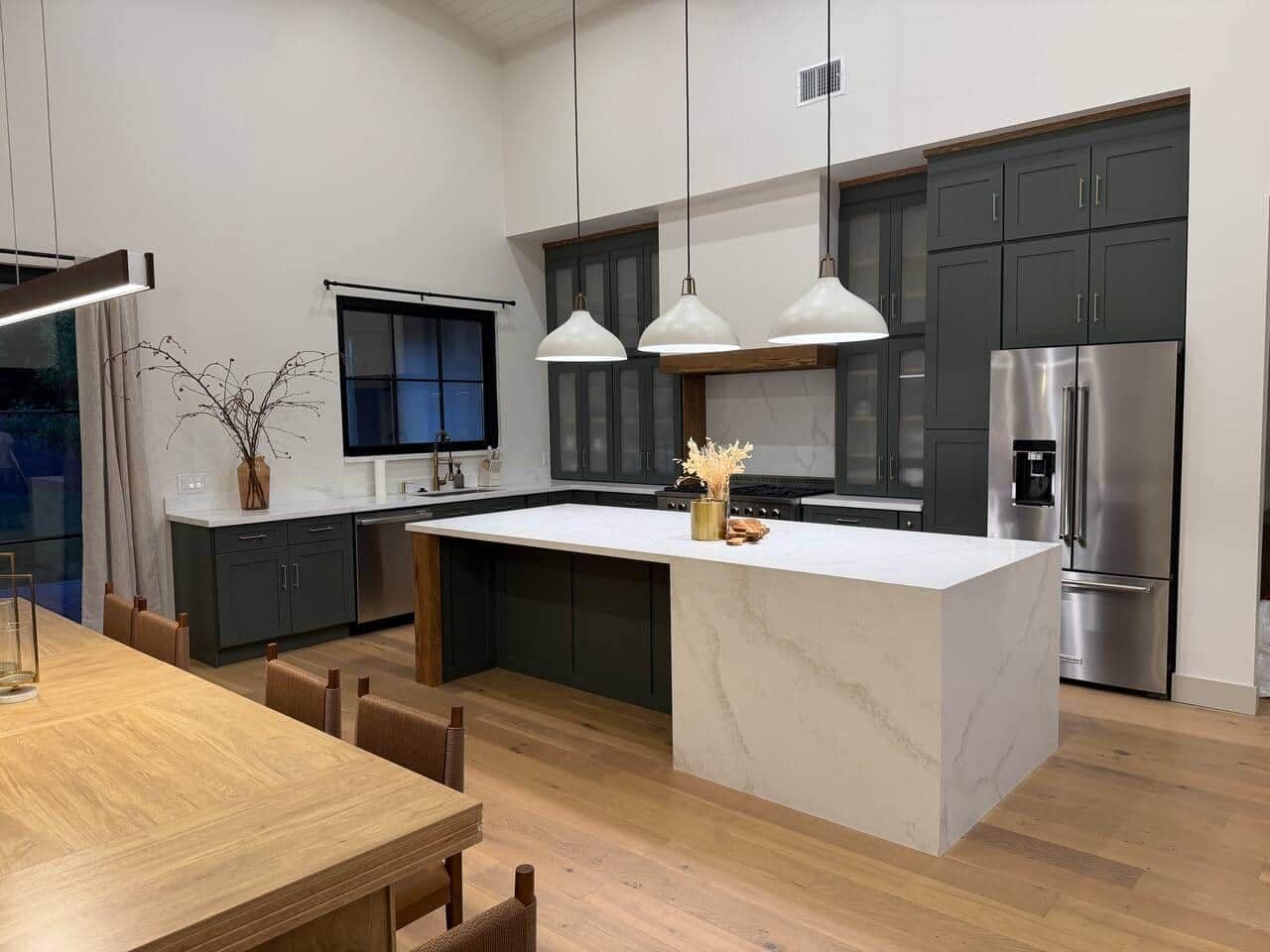 A modern kitchen with a central island, dark cabinets, stainless steel appliances, and pendant lighting.