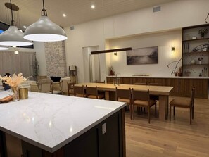 Une cuisine moderne dotée d’un grand îlot central, de luminaires suspendus et d’un coin repas avec des meubles en bois.