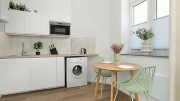 Een moderne keuken met een ingebouwde wasmachine, een eethoek met een tafel en stoelen, en een raam met een plant.
