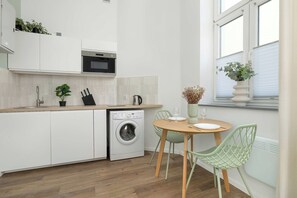 Een moderne keuken met een ingebouwde wasmachine, een eethoek met een tafel en stoelen, en een raam met een plant.