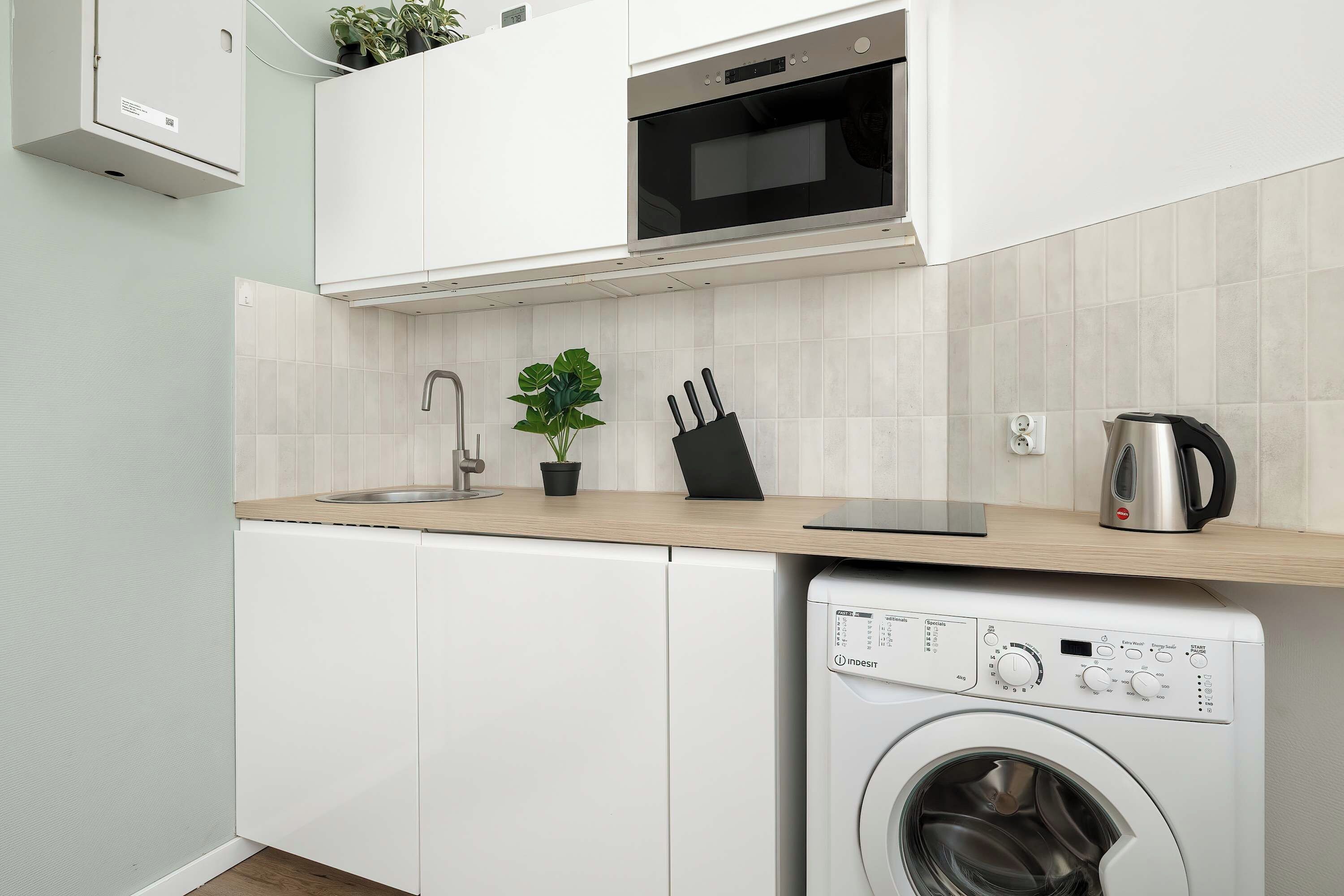 A compact kitchen with a built-in washing machine, a microwave, and a sink.