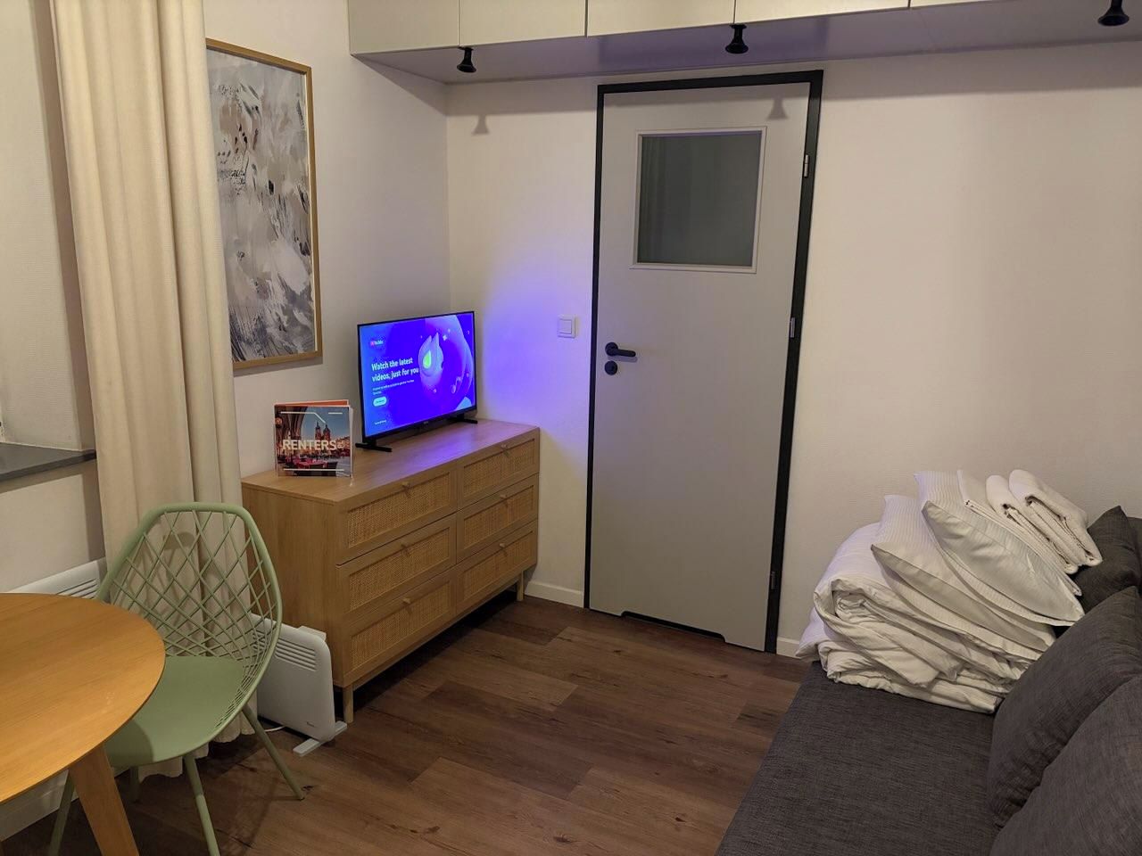 Een kleine kamer met een bed, een kaptafel, een televisie en een deur.