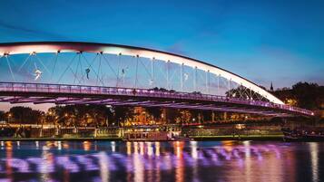 Een brede, verlichte brug over het water, met een stadsgezicht op de achtergrond.