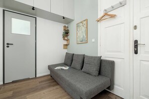 Een kamer met een grijze bank, een witte deur en een wandplank met een plant.