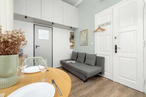 A modern living room with a dining area, grey sofa, white doors, and a hanging plant. - Cracow | Celna 1 | Cosy Studio | Air conditioning (Kraków)