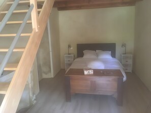 A bedroom with a wooden bed, a nightstand, a lamp, and a staircase. - Cottage 'L'entredeux' with Shared Terrace, Shared Garden and Wi-Fi (Saint-Viaud)