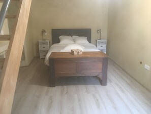 A bedroom with a bed, bedside tables, a nightstand, a wooden bench, and a staircase. - Cottage 'L'entredeux' with Shared Terrace, Shared Garden and Wi-Fi (Saint-Viaud)