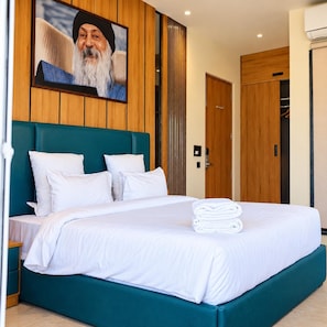 A hotel room with a large bed, wooden paneling, a teal headboard, and a framed picture above the bed. - Shree Rajneesh Osho Ashram (Rishikesh)