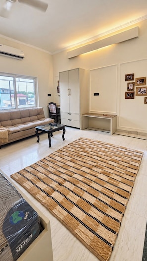 A living room with a large striped rug, a sofa, a coffee table, and a cabinet. - Shree Rajneesh Osho Ashram (Rishikesh)
