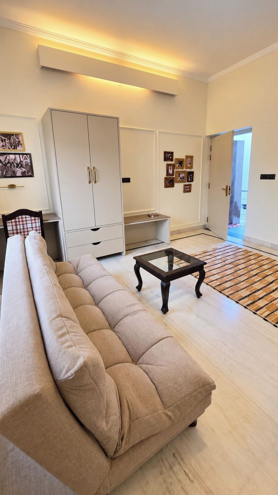 A living room with a sofa, a coffee table, a wardrobe, and a door leading to another room.