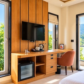 A modern bedroom with a wooden desk, a television, a small refrigerator, and a chair. - Shree Rajneesh Ashram (Rishikesh)