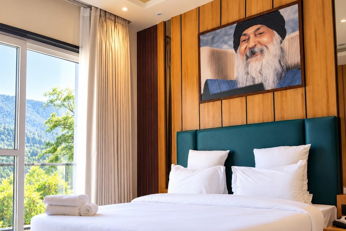 A large bed with white bedding, a teal headboard, and a wooden panel wall with a framed picture.