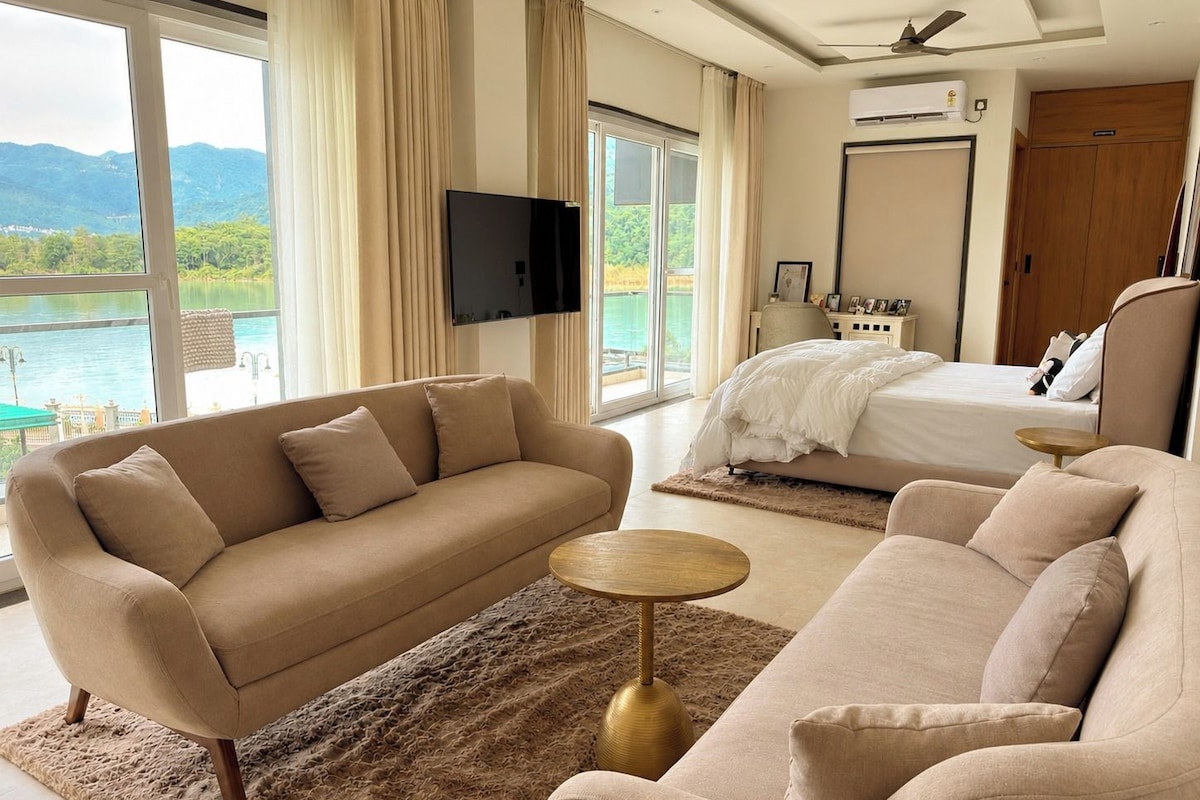 A hotel room with a sofa, a bed, a TV, and a view of a lake.