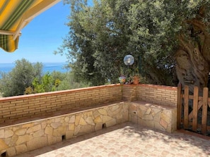 A stone bench area with a view of the sea, a potted plant, and a wooden fence.