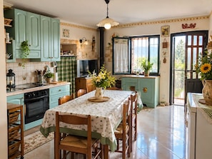 Una cucina con mobili color petrolio, un tavolo da pranzo con sedie e una finestra vista.