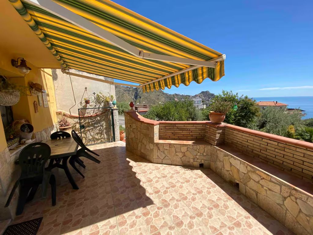 Un balcon avec un mur en pierre, une table avec des chaises et un auvent jaune à rayures.